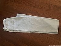 Folded light blue denim jeans showing front pocket, belt loops, and button with rivets on the pocket edges.