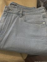 Close-up of the front pocket, belt loop, and button area of the R brand jeans showing light blue denim fabric.