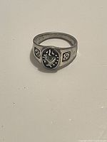 Close-up image of sterling silver ring with raised ornate oval centerpiece and side accents, showing front view.