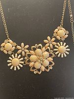 Close-up view of the gold tone floral necklace showcasing cream enamel petals and embedded Swarovski crystals on a gold tone chain.