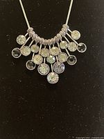 Close-up front view of the silver-tone chain necklace with pendant showing multiple round faceted clear Swarovski crystals in metal settings against a black background.