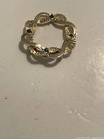 Front view of vintage gold-tone brooch with green stones on a flat surface.