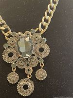 Close up of vintage style necklace pendant showing large central faceted gem and detailed beadwork with dangling circular charms.