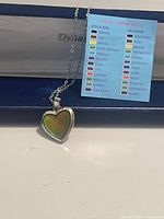 Photo of the silver-tone heart charm necklace on a chain with a card showing mood ring color meanings in English and Spanish.