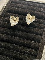 Heart-shaped translucent clip on earrings with pearl-like bead in center placed on black earring display.