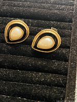 Front view of vintage clip-on earrings showcasing the faux pearl, black enamel and gold-tone metal with rope detailing.