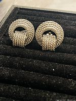 Pair of vintage silver tone clip-on earrings with a textured woven circular design displayed on black velvet.