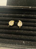 Photo showing front view of a pair of gold tone clip on earrings designed as leaves with textured vein patterns, displayed on black velvet jewelry holder.