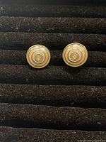 Front view of vintage clip on earrings showing circular concentric pattern in gold tone metal, placed on black velvet.