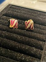 Close-up front view of vintage gold plated clip-on earrings with red and white enamel decorative wave pattern on display tray