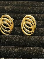 Close-up photo of the pair of vintage gold plated clip on earrings with ribbed oval design in a display case.