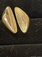 Pair of vintage gold plated clip-on earrings shown on black fabric surface, displaying smooth polished exterior and textured interior.