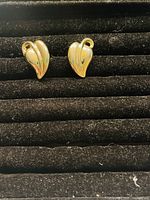 Front view of the pair of gold plated leaf shaped clip-on earrings shown lying flat on black textured surface.