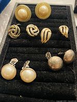 Multiple pairs of vintage clip-on earrings with faux pearl and gold-tone metal designs arranged on black display