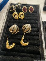 Top view of six pairs of vintage clip-on earrings in a black display tray showing variety of designs and materials