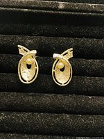 Front view of the vintage clip-on pearl earrings showing gold-tone oval open design with a pearl inside and bow accent on top on black display pad.