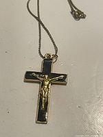 Photo of vintage gold plated crucifix cross pendant necklace with black enamel detail, showing the entire pendant and part of the chain on a white surface.