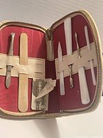 Open nail care kit showing mother of pearl manicure tools secured inside with elastic straps and small razor blades included.