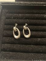 Pair of vintage silver-tone screw on earrings placed in black jewelry tray, showing front view of earring design and clip closure.