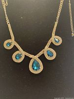 Full view of the gold-tone Swarovski crystal necklace with five blue teardrop crystal pendants on a black background.