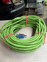 Green heavy duty extension cord coiled on table, showing blue 3-prong grounded plug and cable wear
