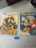 Lot of two vintage comic books laid side by side on a flat surface, protected in plastic sleeves. Left comic is Walt Disney's Comics and Stories featuring Mickey Mouse on cover. Right comic is Bugs Bunny with Looney Tunes characters on colorful cover.