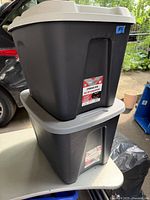 Two stacked black storage totes with gray lids, with label clearly visible on the front of the top tote.