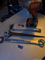 Photo showing the Milwaukee 18V cordless drill with battery alongside three wrenches on a table.