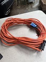 Photo of coiled orange 50-foot extension cord on a gray surface with visible three-prong plug end.
