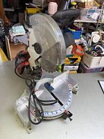 Metal base and circular blade with power cord lying on the base, showing the saw's front left side.