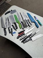 All 19 knives and cleavers arranged on a table showing the variety and condition of cutting tools in the lot.