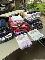 Lot of folded towels in various colors and patterns including two white towels with floral embroidery and lace trim in front
