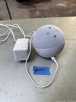 Alexa Echo Dot 5th Generation smart speaker connected to power adapter, shown on table with a blue tape labelled #140
