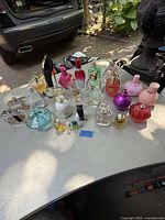 Wide view of multiple perfume bottles in various colors and shapes on table outdoors.