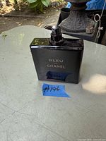 Dark blue rectangular glass bottle of Bleu de Chanel Parfum with spray nozzle, cap removed, on tabletop with blue tape '#196'