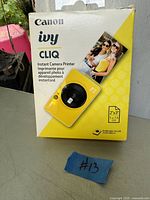 Canon iwy Cliq Instant Camera Printer original boxed packaging in yellow theme showing front and product details.