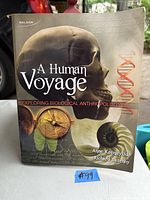 Cover photo of 'A Human Voyage Exploring Biological Anthropology' book showing skull, compass, DNA illustration, author names and publisher brand.