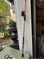 Full view of the orange MAXSTX fishing rod leaning against a wall outdoors on a table surface.