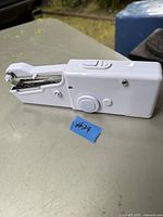 White hand held portable sewing machine Handy Stitch shown from side angle on an outdoor surface.