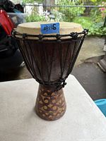 Front angled view of the djembe drum showing the full drum with carved wood base and rope tension system.