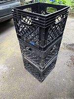 Stack of three black plastic milk crates showing lattice design and handles, with visible normal wear.