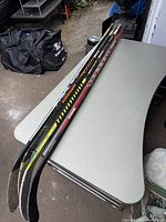 Four left hand hockey sticks laying on a table showing blades and shafts with brand names.