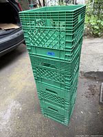 Stack of 4 green plastic milk crates showing lattice sides, handles, and size proportion relative to car trunk.