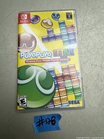 Nintendo Switch game case for Puyo Puyo Tetris showing front cover with colorful puzzle pieces and characters, placed on a flat surface with a blue sticker marked #128.
