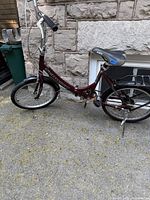 Full side view of burgundy Schwinn folding bicycle showing frame, wheels, handlebars, black saddle, and rear rack.