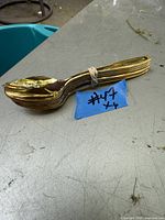 Six gold plated tea spoons stacked and bound by a rubber band on a gray surface.