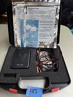 TENS 3000 device with electrode wires and instructional papers inside black foam carrying case.