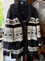 Front view of a unisex knit cardigan in black and white Nordic pattern with button detail and pockets.