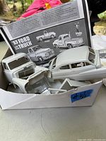 Unassembled gray plastic body parts for the 1953 Ford pickup and 1951 Mercury inside a damaged white box along with an instruction sheet.
