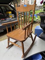 Front and side angle of vintage oak kids rocking chair showing wood grain, spindle back, armrests, and rocker legs.